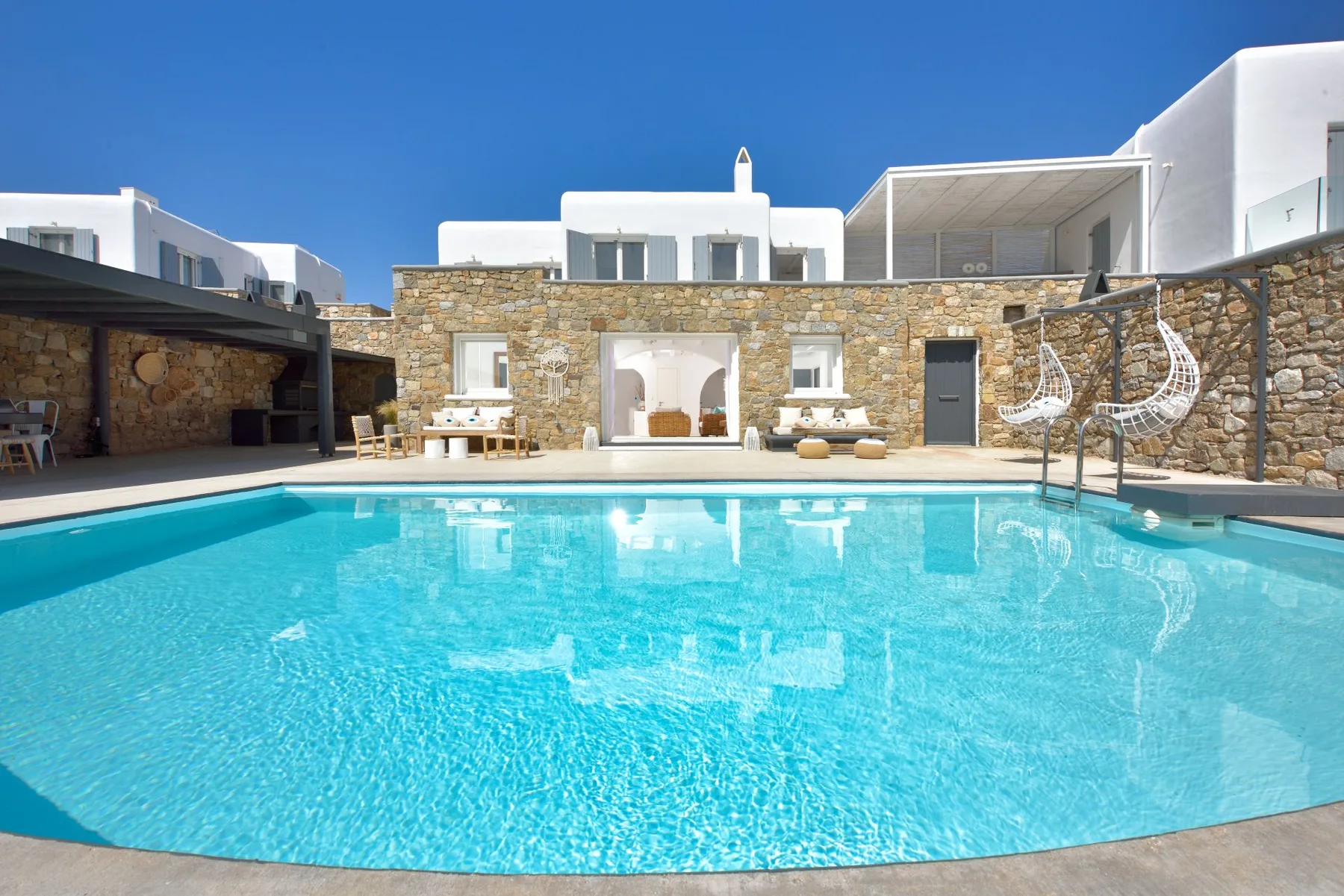 A turquoise swimming pool sits in front of a stone courtyard and white buildings.