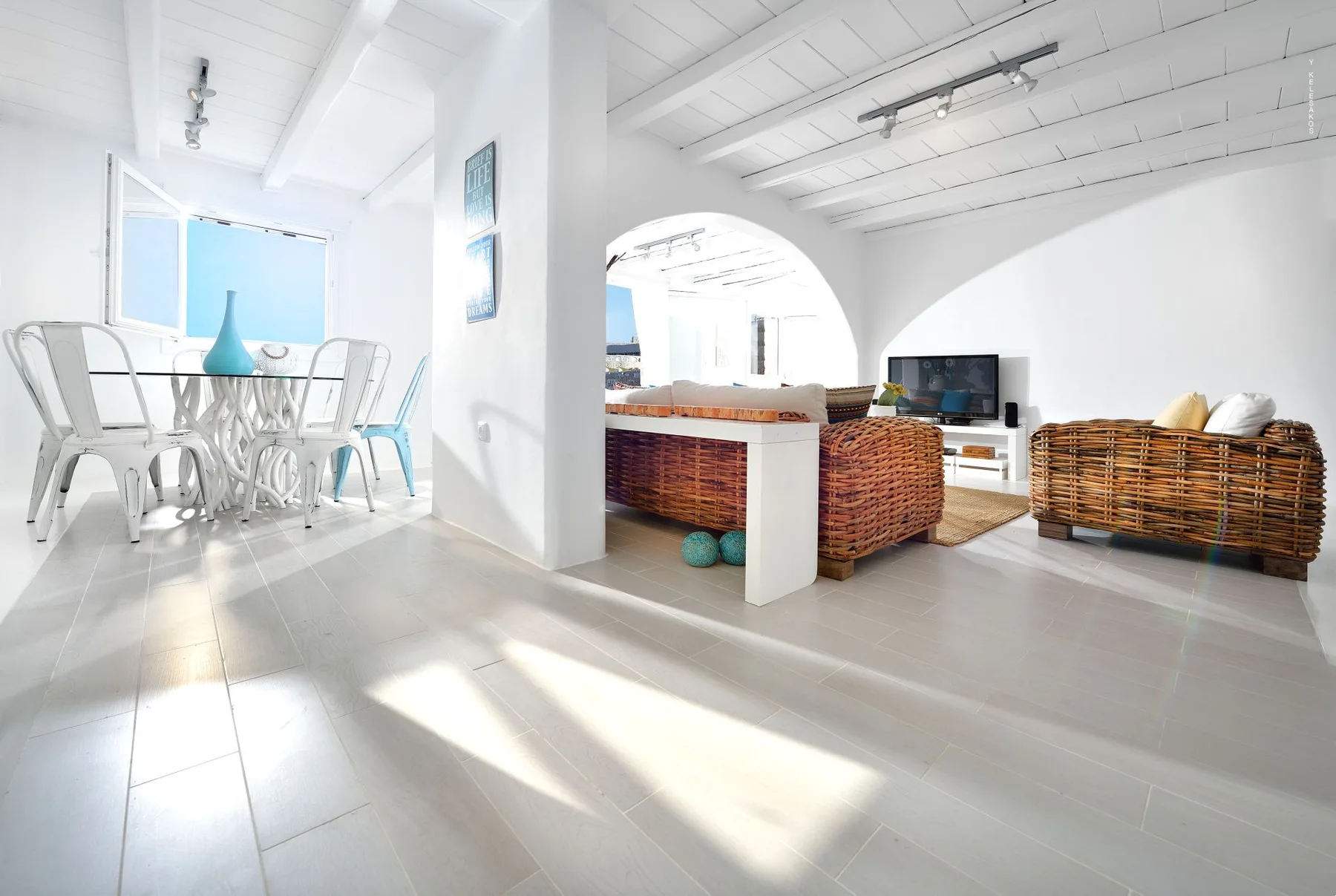 A bright open-plan living and dining area with wicker seating and a glass dining table.