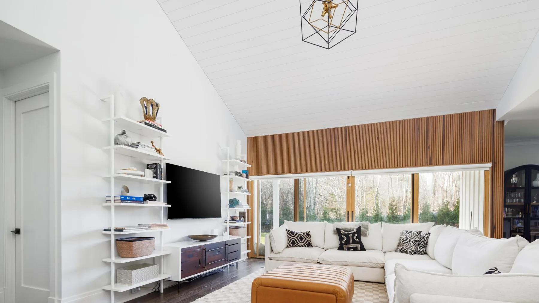 A bright living room with white seating, a television, and large windows.