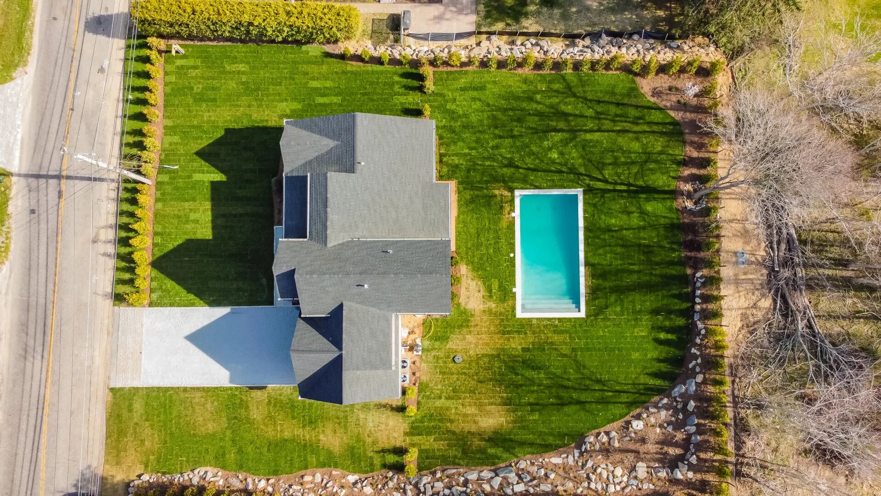 An aerial view shows a house surrounded by a lawn, garden beds, and a swimming pool.
