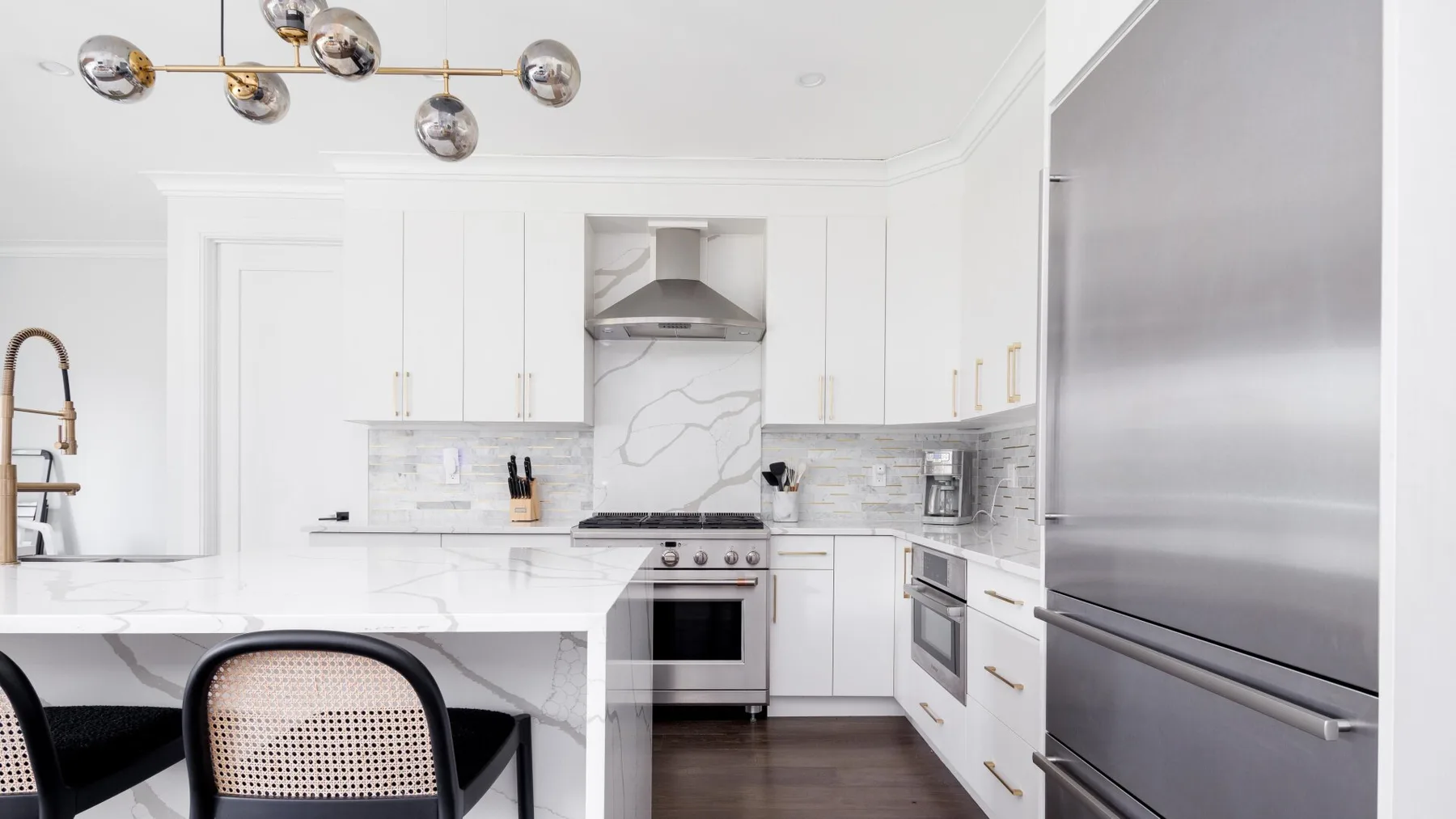 A bright white kitchen with a central island, stainless steel appliances, and marble-patterned backsplash.