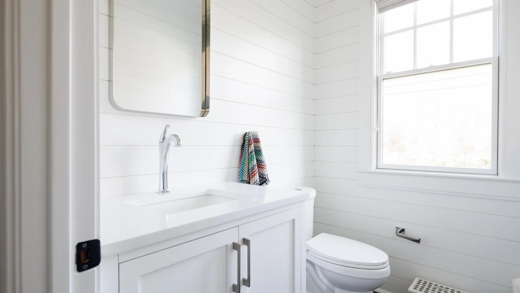A bright bathroom with a white vanity and toilet beneath a window.