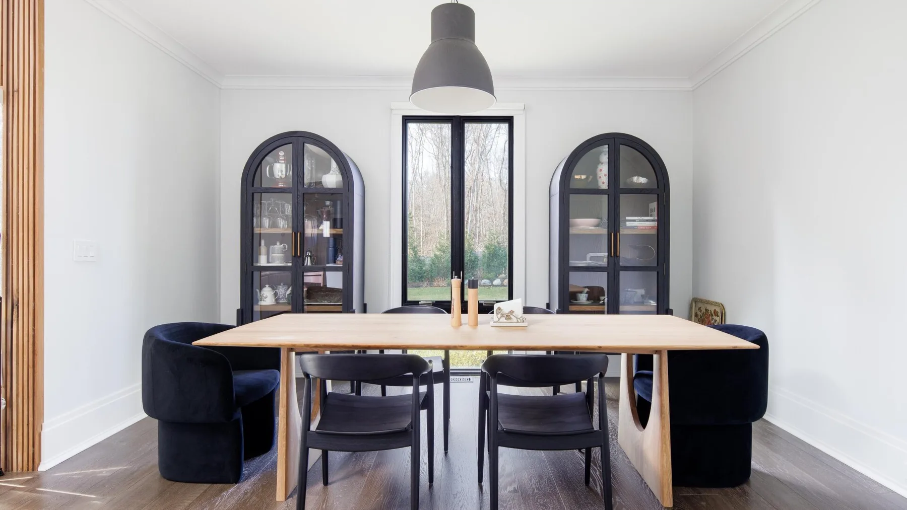 A bright dining room with a long table, dark seating, and tall windows.