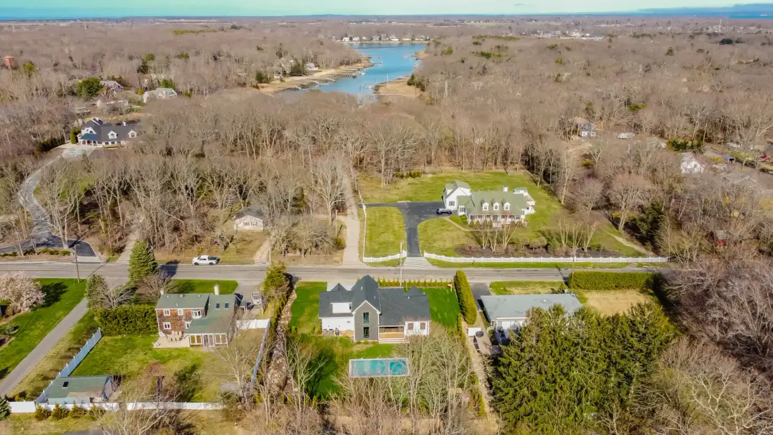 Aerial view of homes surrounded by wooded land, with a river in the distance.