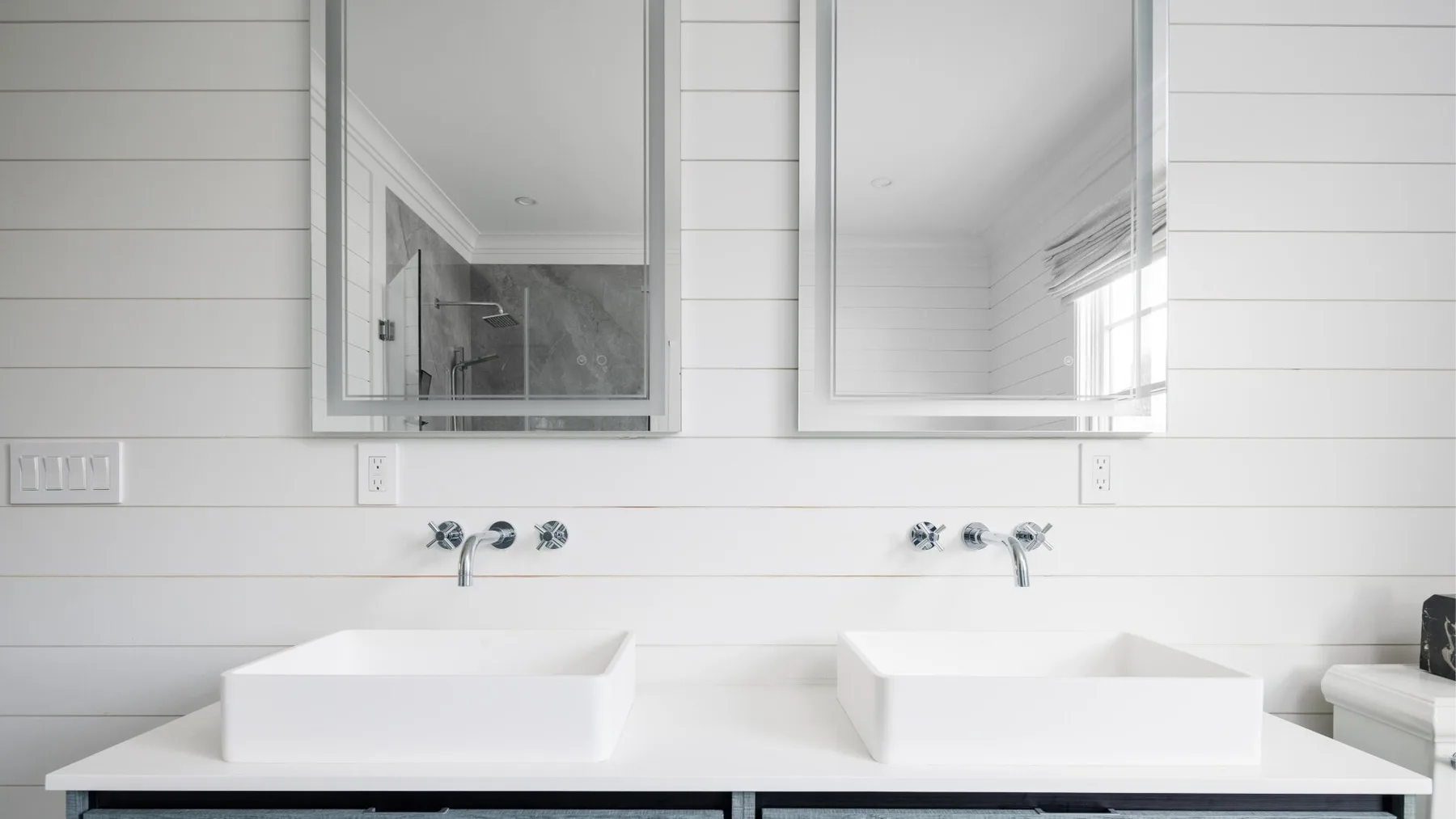A bright bathroom vanity with two white vessel sinks and wall mirrors.