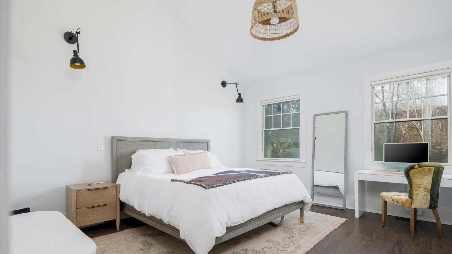 A bright bedroom with a bed, bedside table, and desk by the window.