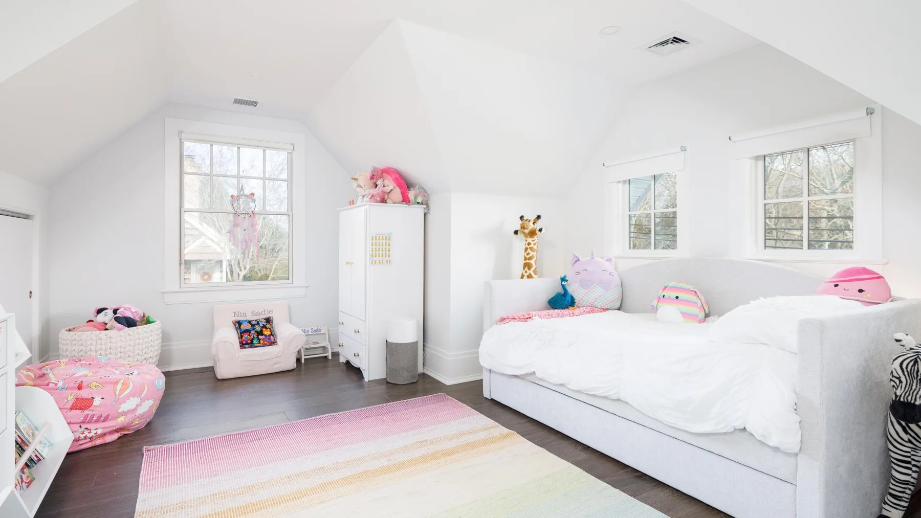 A bright bedroom with white beds, colorful bedding, and a pastel striped rug.