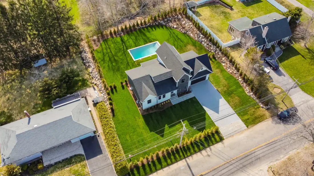 An aerial view of a house with a rectangular swimming pool in a green yard.