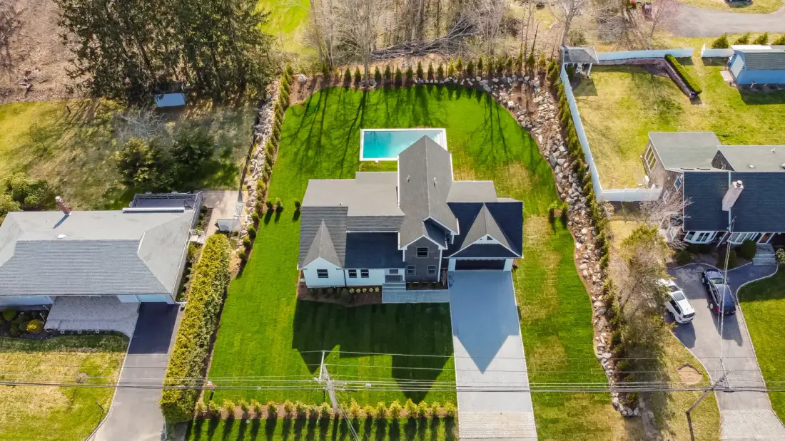 An aerial view shows a house, a green lawn, and a small pool.