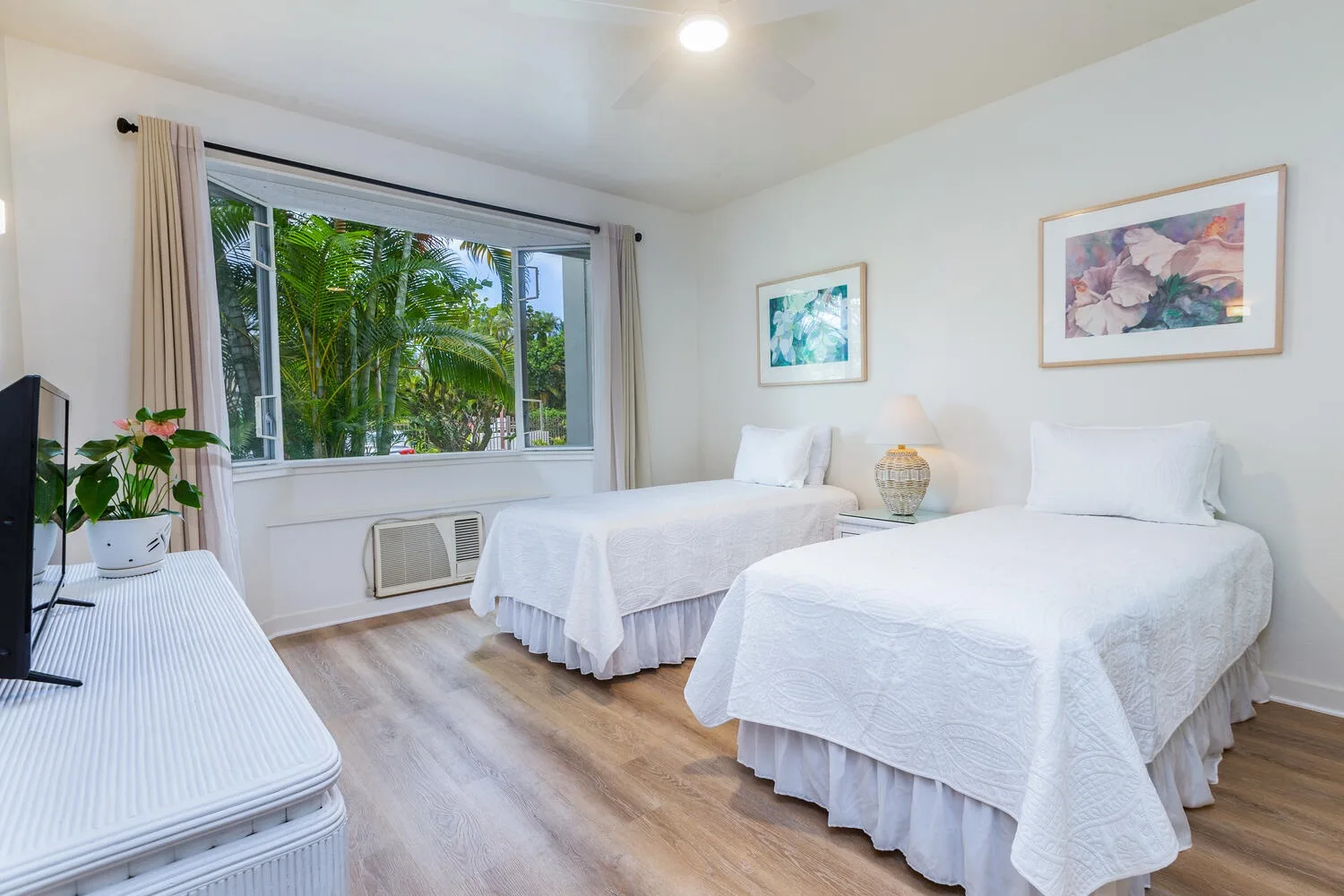 Un dormitorio luminoso con dos camas y una ventana grande que da a la vegetación.