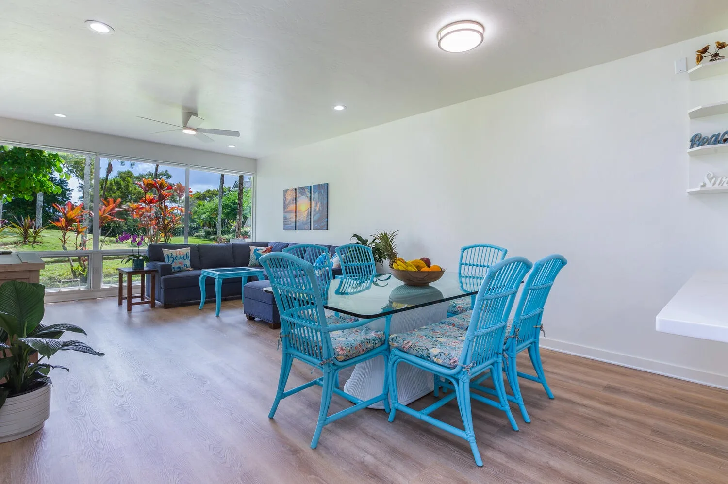 Una luminosa sala de estar y comedor con asientos azules y grandes ventanas hacia la vegetación.