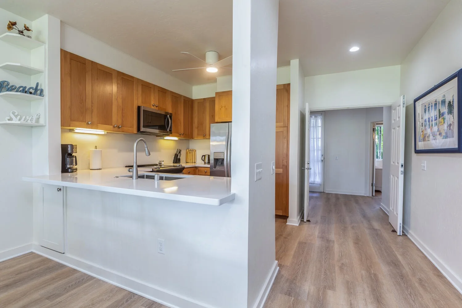 Cocina abierta y pasillo con gabinetes de madera y piso de tono claro.