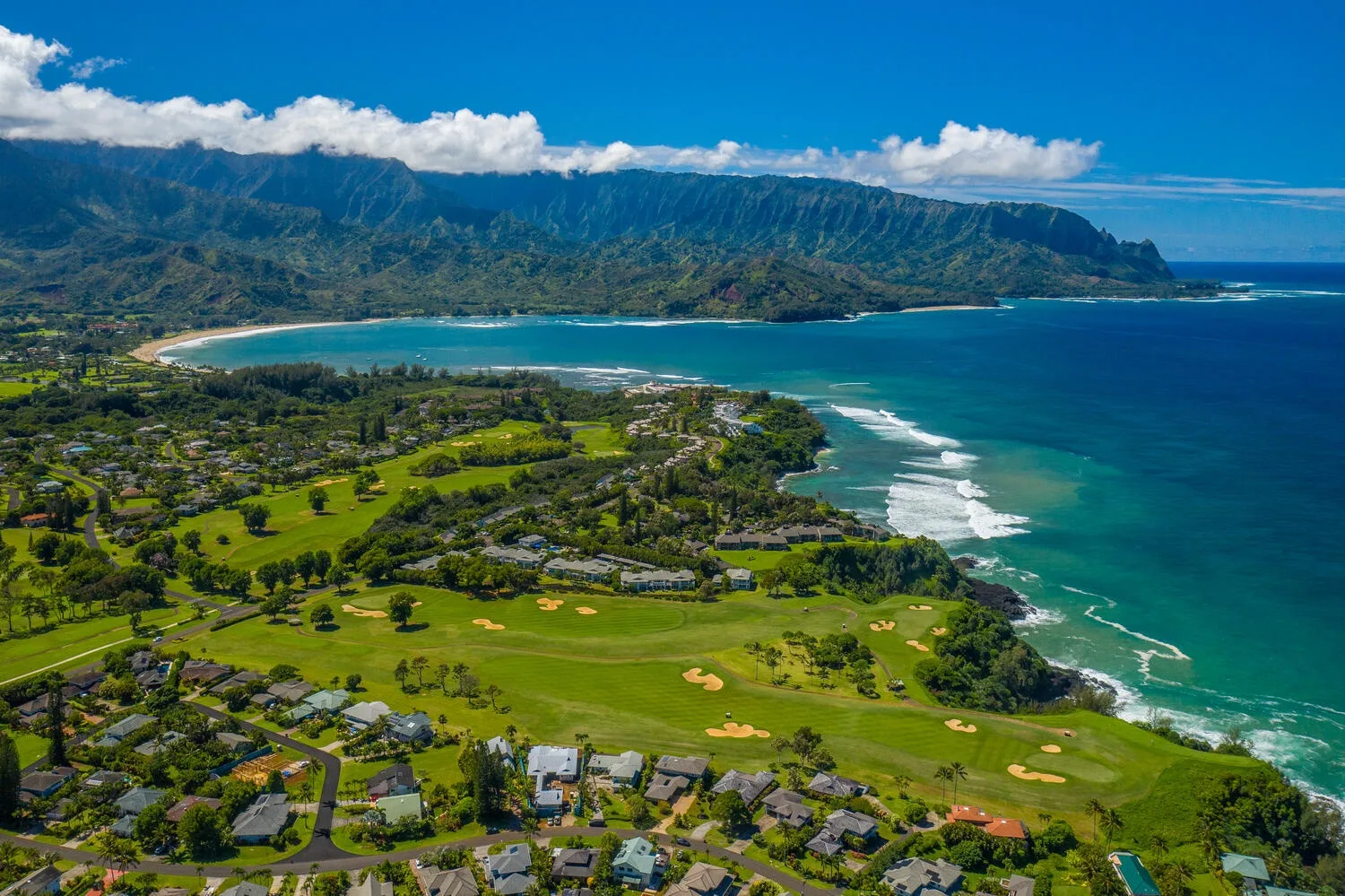 Paisaje costero con campos verdes, viviendas y una amplia bahía oceánica.