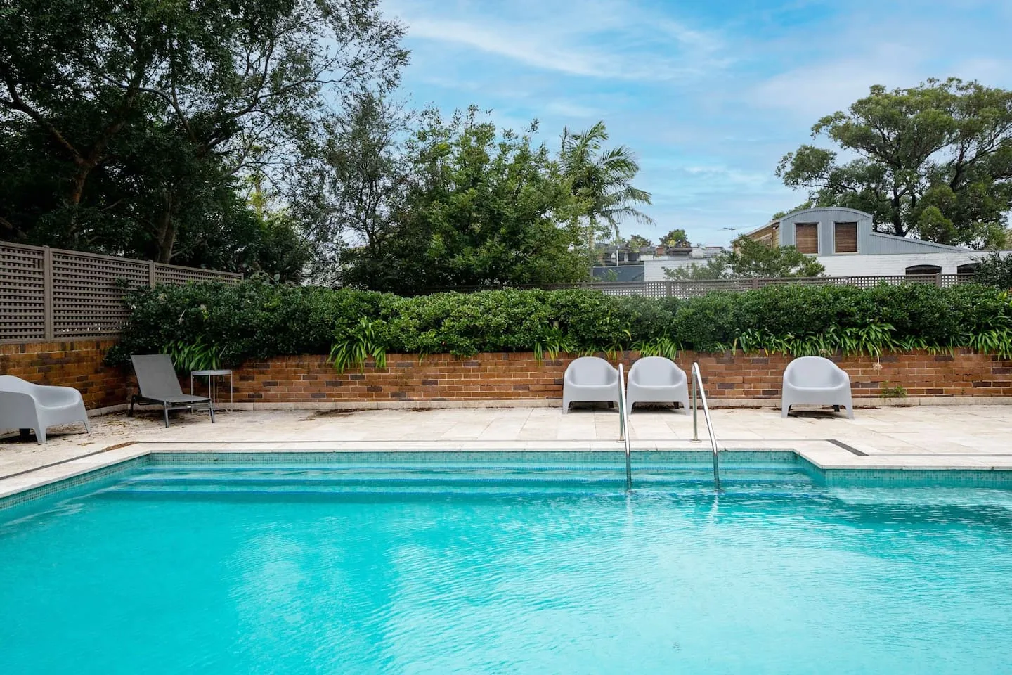 An outdoor swimming pool bordered by a paved deck and lounge seating.