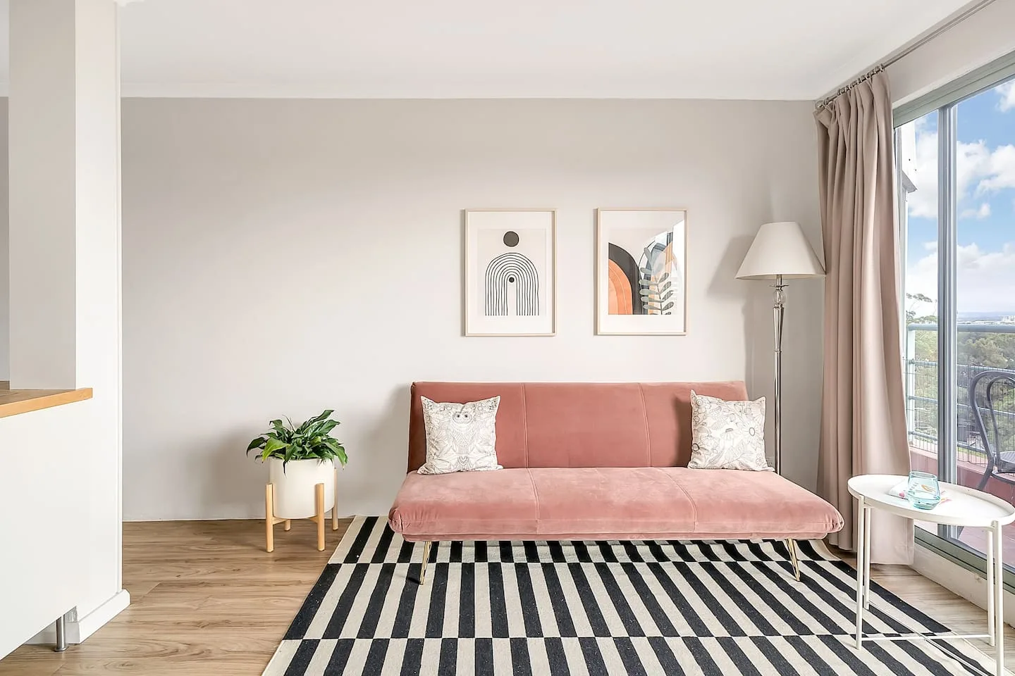 A living room with a pink sofa, framed prints, and a striped rug.