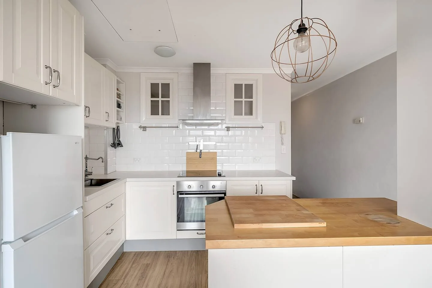 A bright white kitchen has a wooden island and stainless steel appliances.