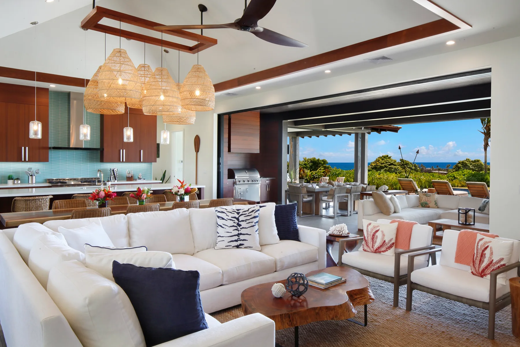 Una sala y comedor de concepto abierto tiene asientos blancos junto a una cocina y vistas al exterior.