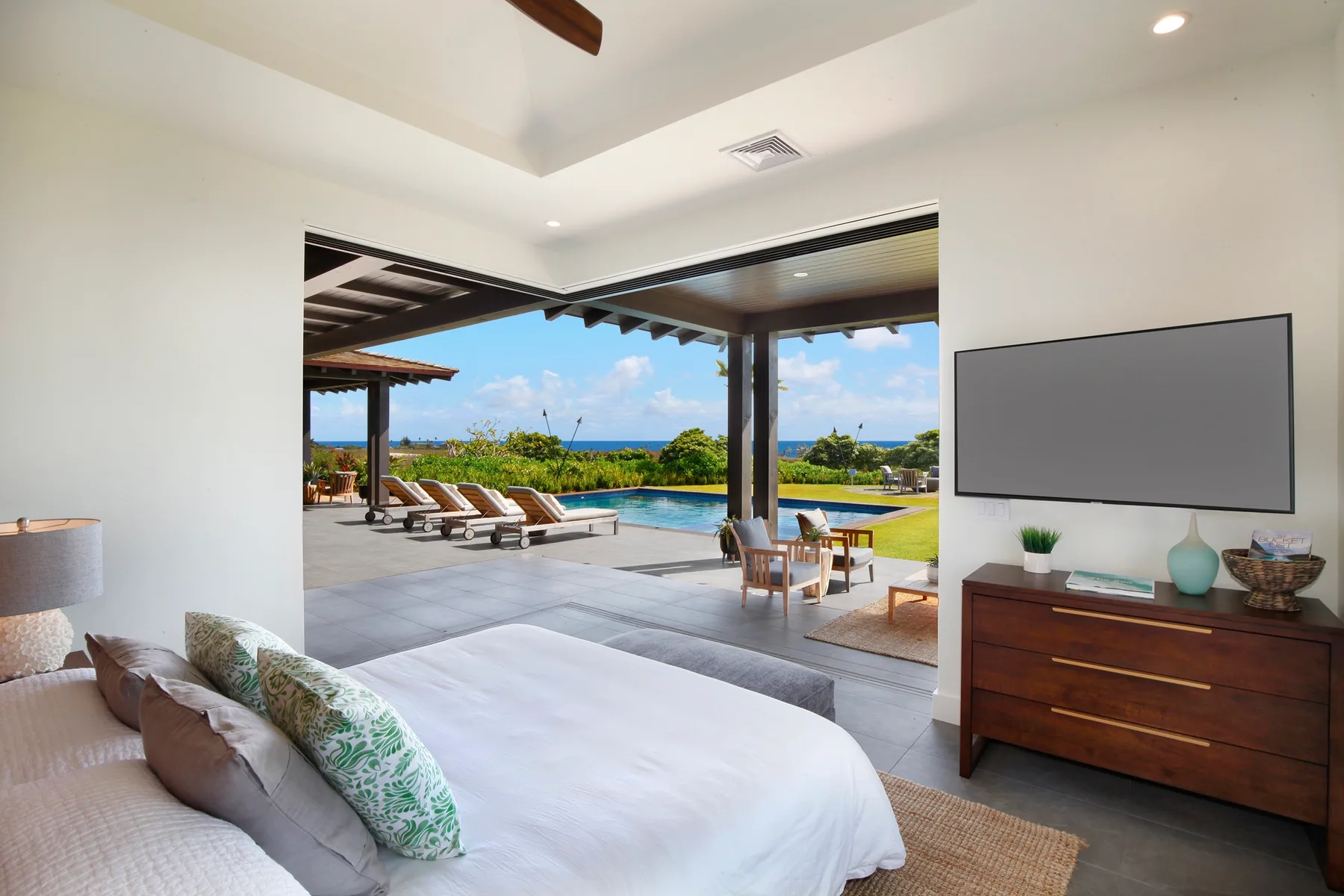 Un dormitorio se abre a un patio cubierto con asientos y vistas a la piscina y al mar.