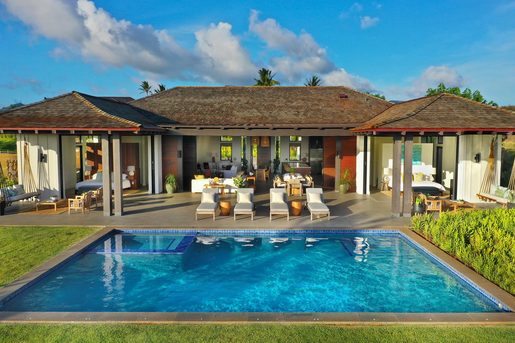 Una villa tropical da a una piscina, con asientos al aire libre en el patio.