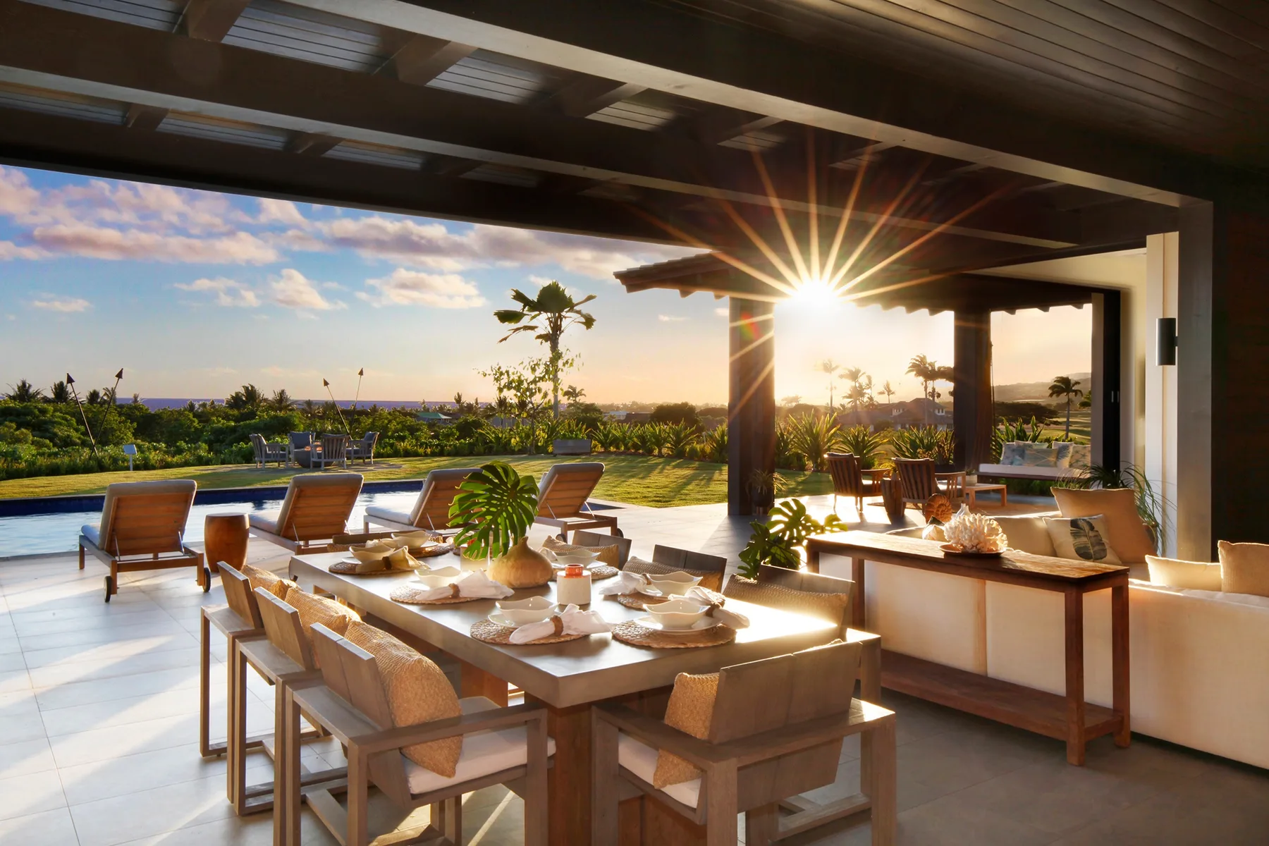 Un comedor al aire libre da a una piscina y jardines con la luz del atardecer.
