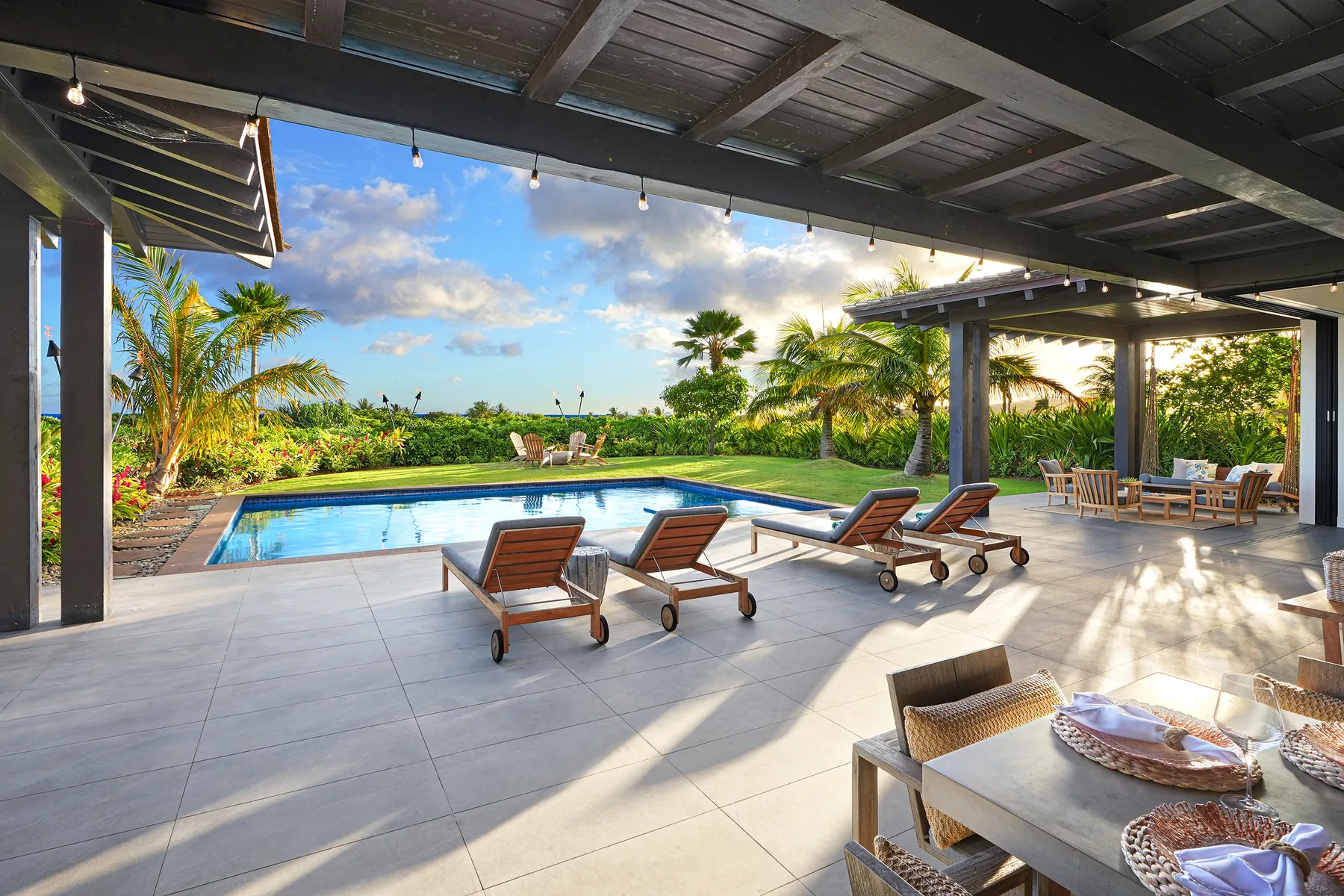 Un patio cubierto da a una piscina, con tumbonas y asientos al aire libre.