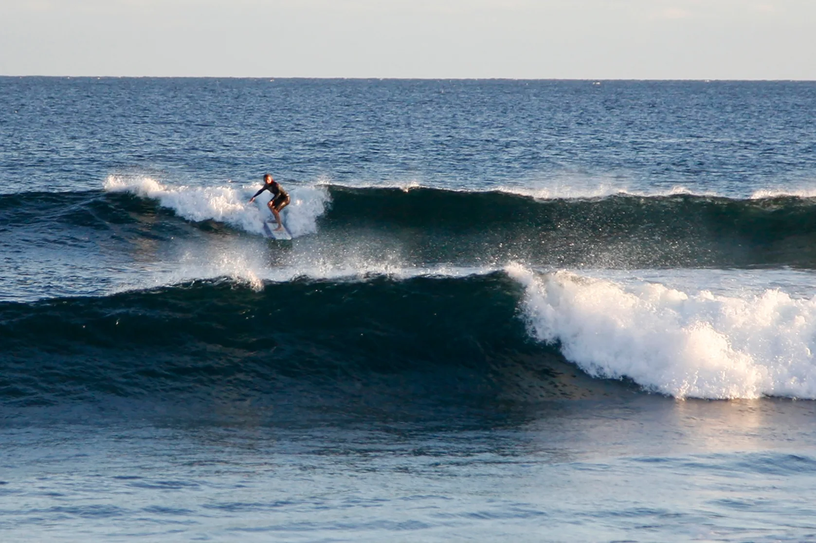 Una persona surfea una ola rompiente en mar abierto.