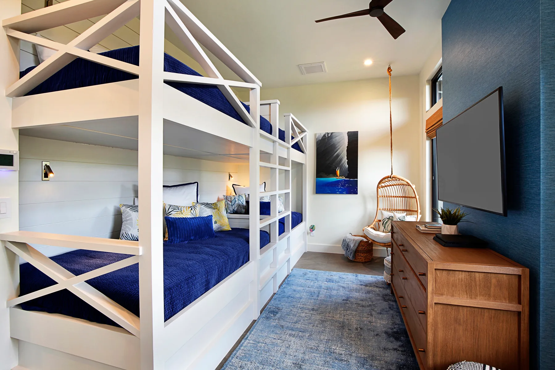 Un dormitorio con literas blancas, ropa de cama azul y una cómoda de madera.