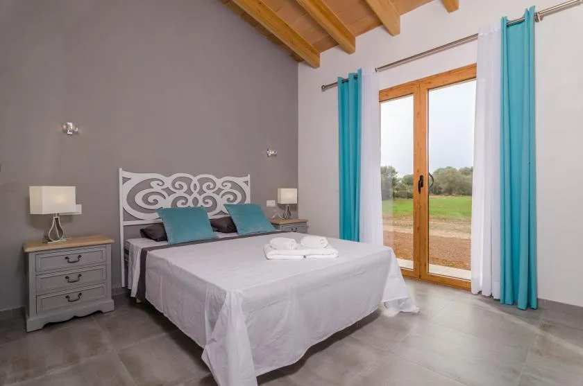 Un dormitorio con cama doble, cabecero decorativo y puertas de vidrio con vistas verdes.