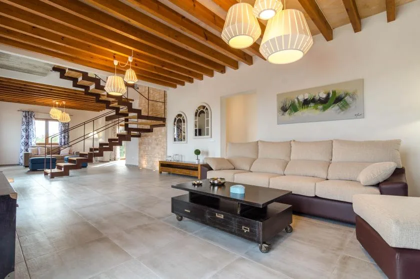 Una amplia sala de estar con un sofá largo, una mesa de centro y vigas de madera expuestas.