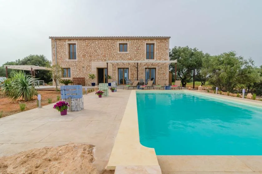 Una casa de piedra está junto a una piscina y una terraza pavimentada.