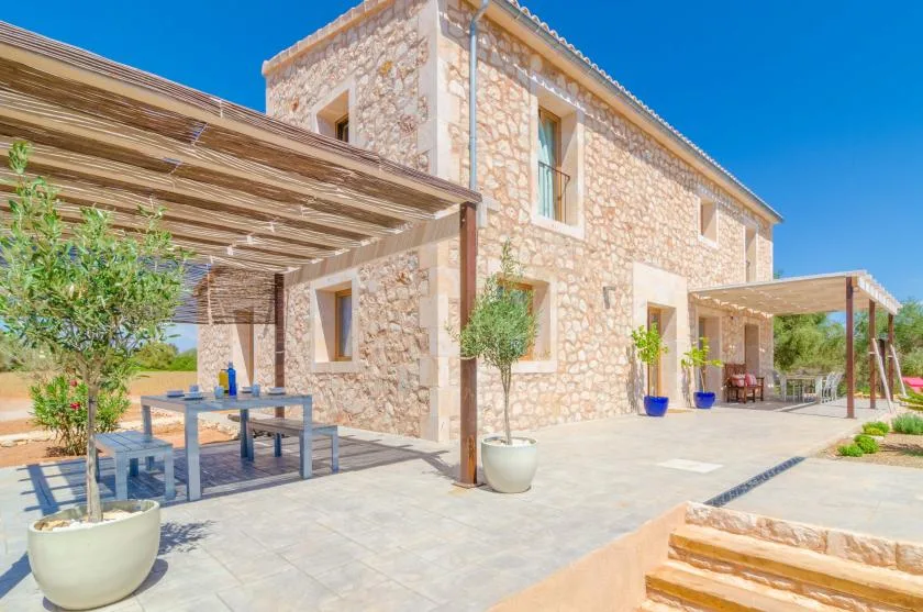 Exterior de una casa de piedra con patio sombreado y asientos al aire libre.