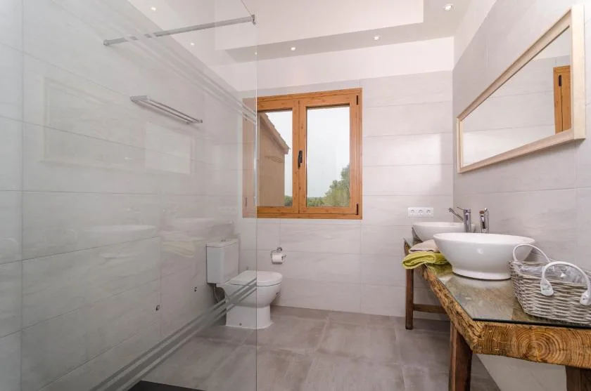 Un baño luminoso con ducha de vidrio, inodoro y lavabo bajo una ventana.