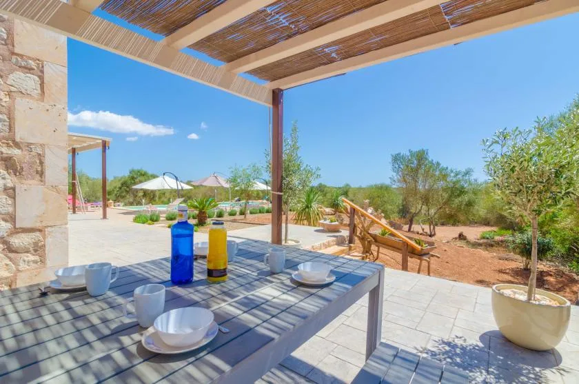 Un comedor en un patio exterior da a un jardín bajo una pérgola sombreada.