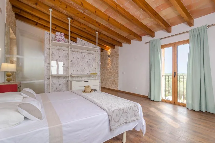 Un dormitorio con ropa de cama blanca, vigas de madera expuestas y una puerta de cristal que da a un balcón.