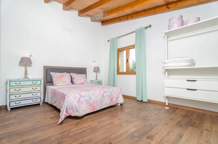 Un dormitorio con una cama junto a una ventana enmarcada por cortinas claras.