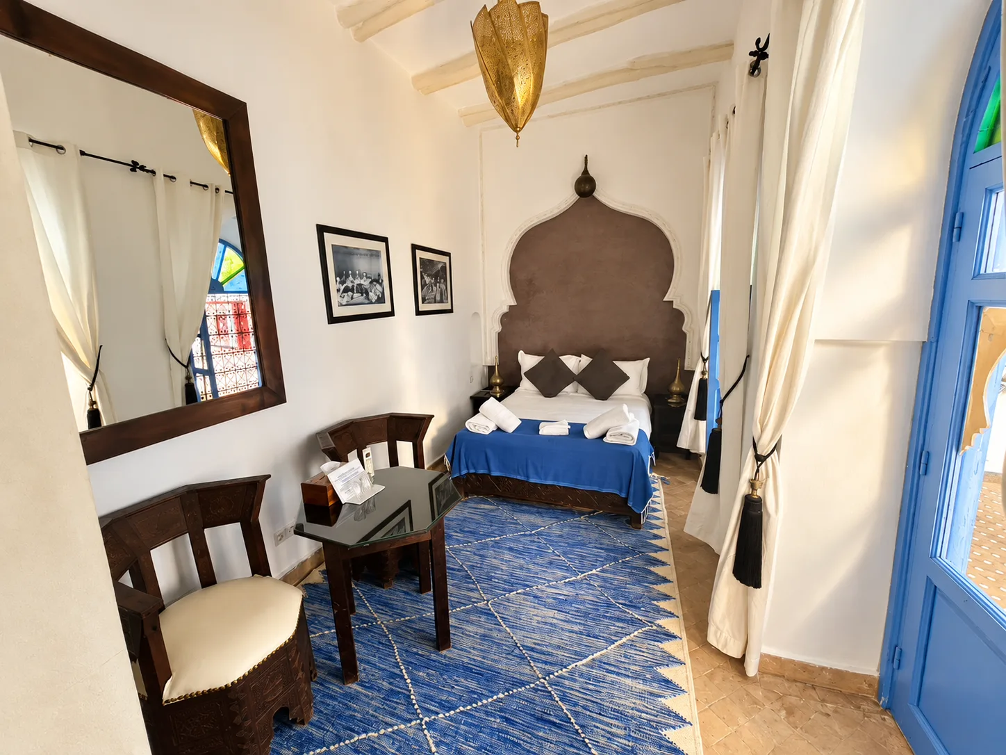 Dormitorio con una colcha azul, sillas y una alfombra estampada