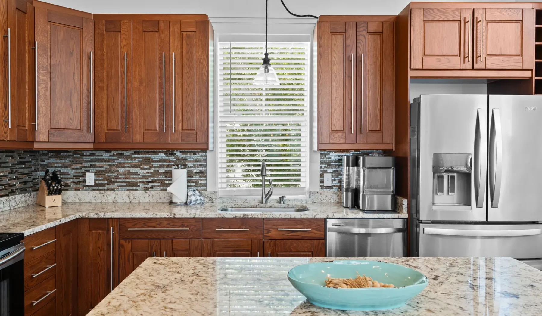 Una cocina con gabinetes de madera, electrodomésticos de acero inoxidable y una gran isla de piedra.