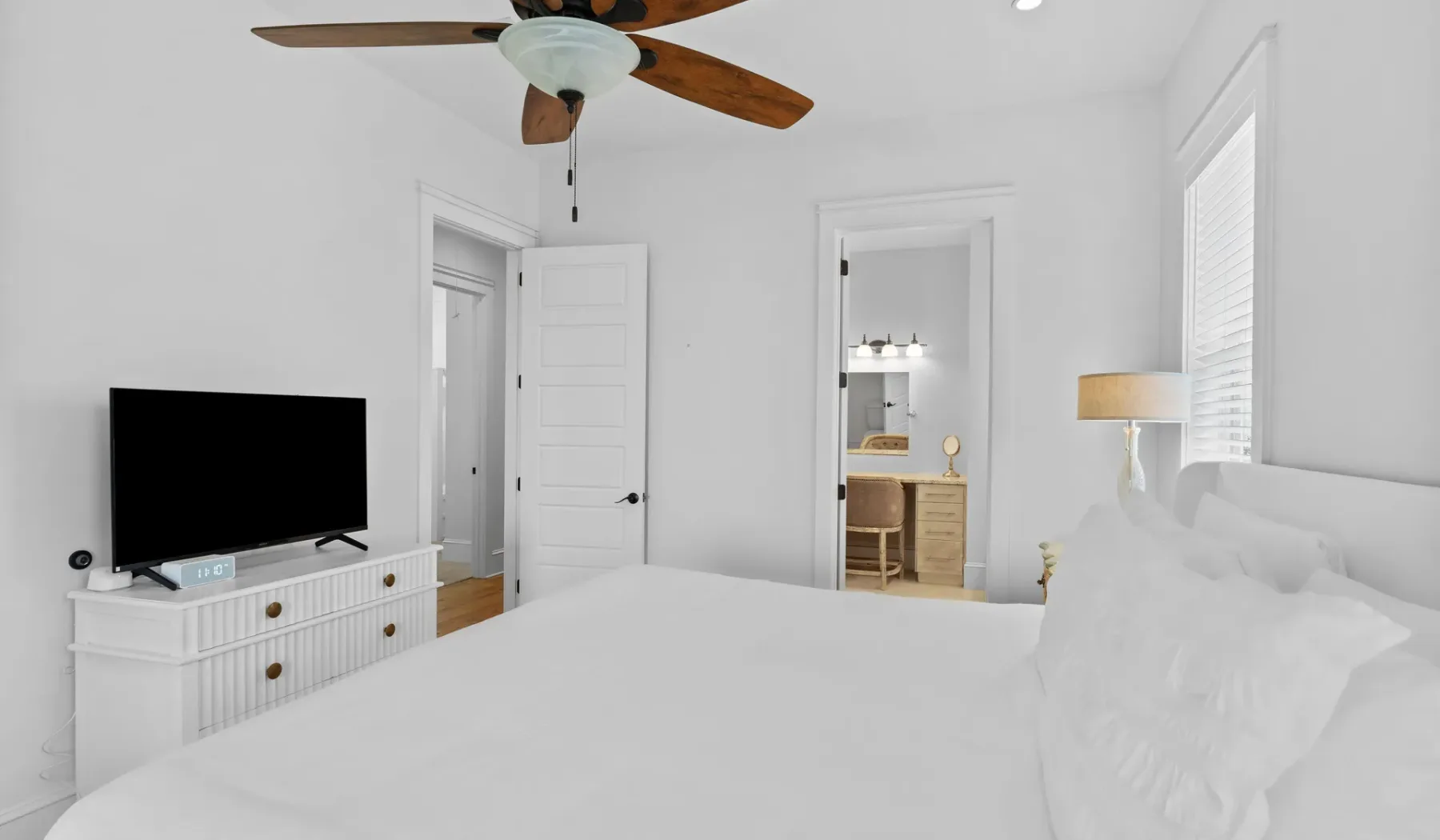 Un dormitorio luminoso con una cama tendida, un televisor y un ventilador de techo.