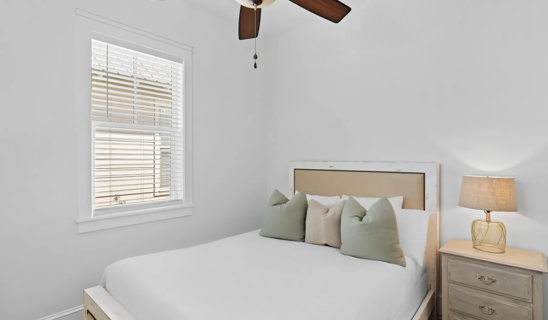 Un dormitorio luminoso con una cama bien hecha y una ventana con persianas.