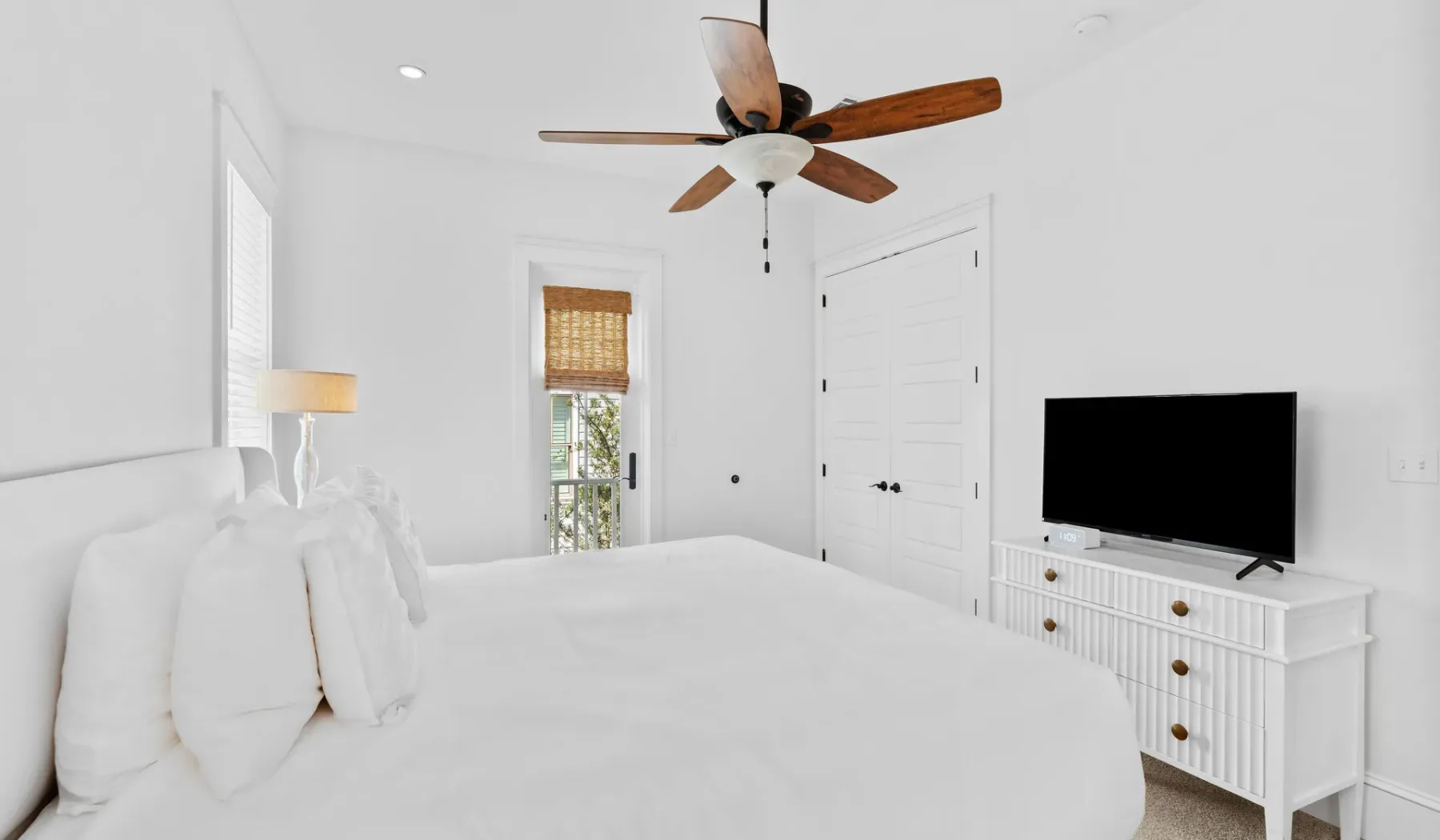 Un dormitorio luminoso con ropa de cama blanca y un televisor sobre una cómoda.