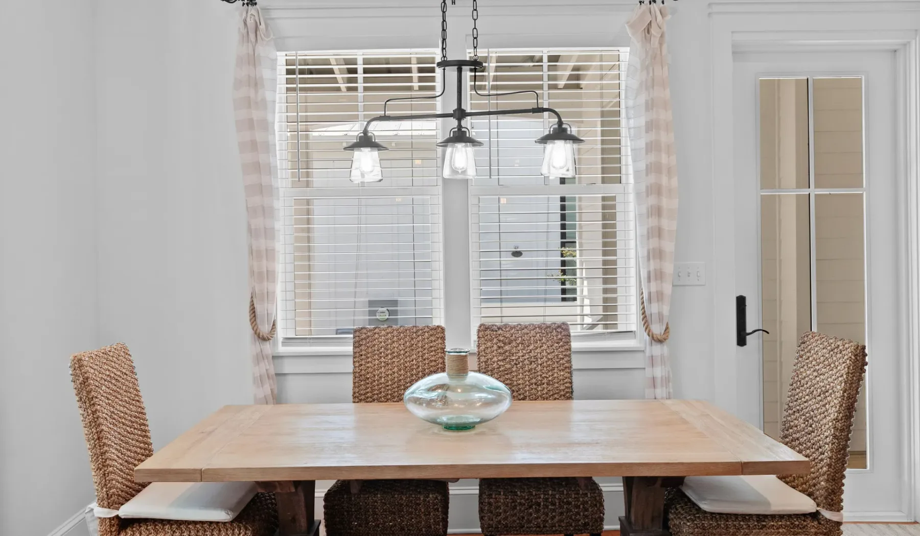 Un comedor con una mesa de madera y asientos tejidos bajo lámparas colgantes.