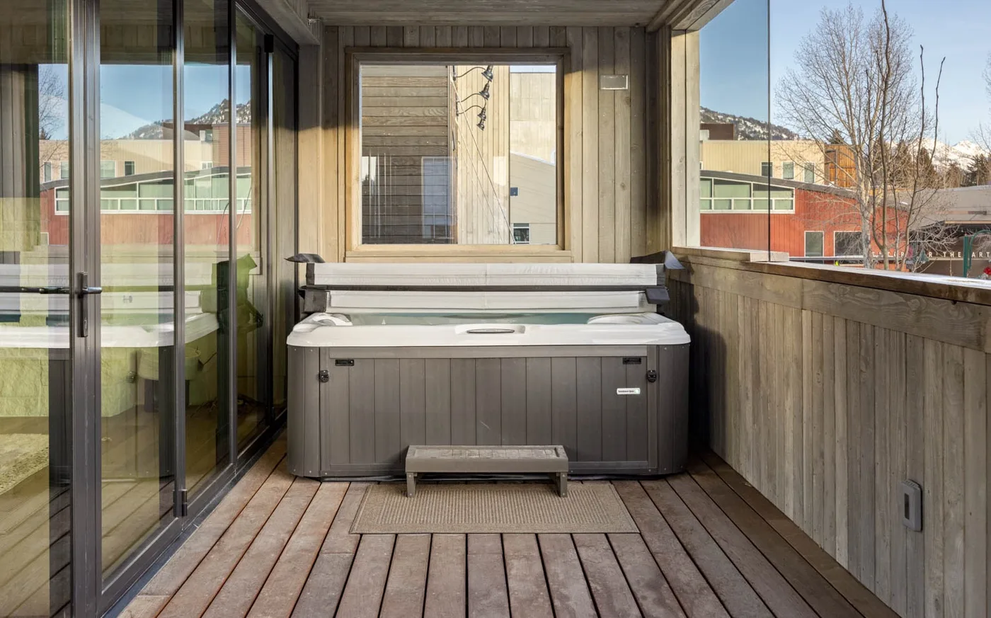 Una terraza exterior cubierta tiene una bañera de hidromasaje junto a grandes puertas de vidrio.