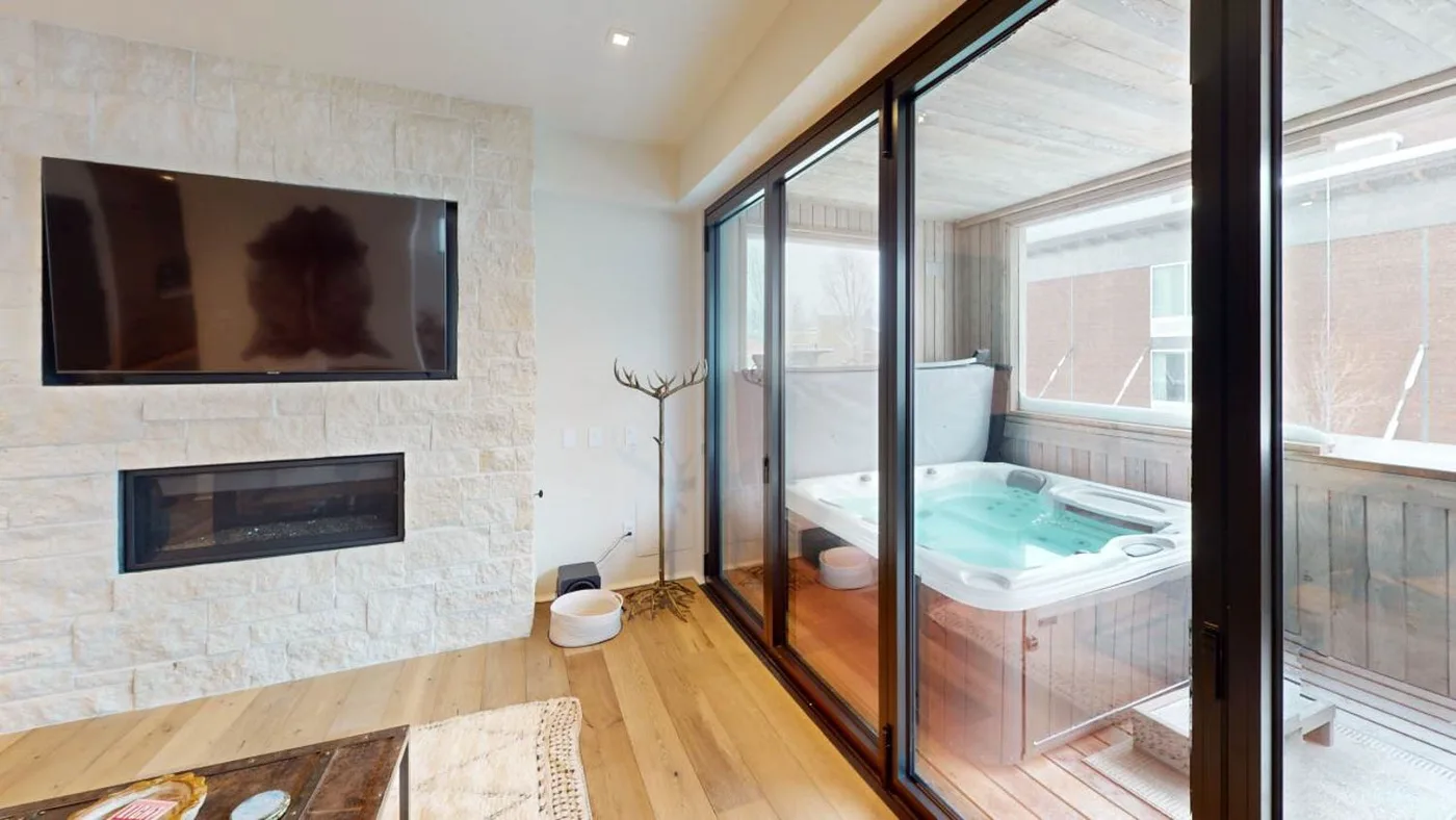 Una sala de estar con un televisor en la pared junto a una bañera de hidromasaje acristalada.