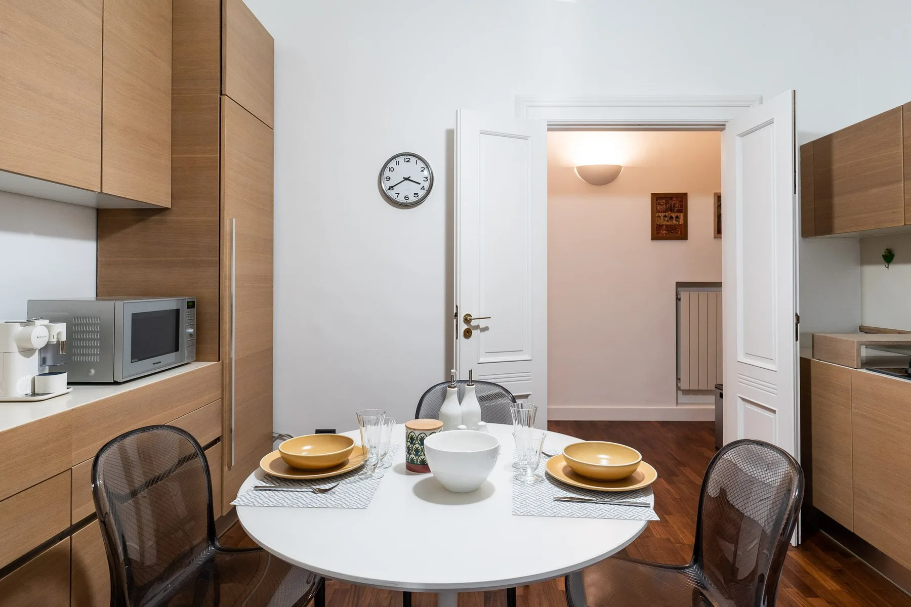 Un comedor con la mesa puesta junto a una puerta abierta que da a un pasillo.