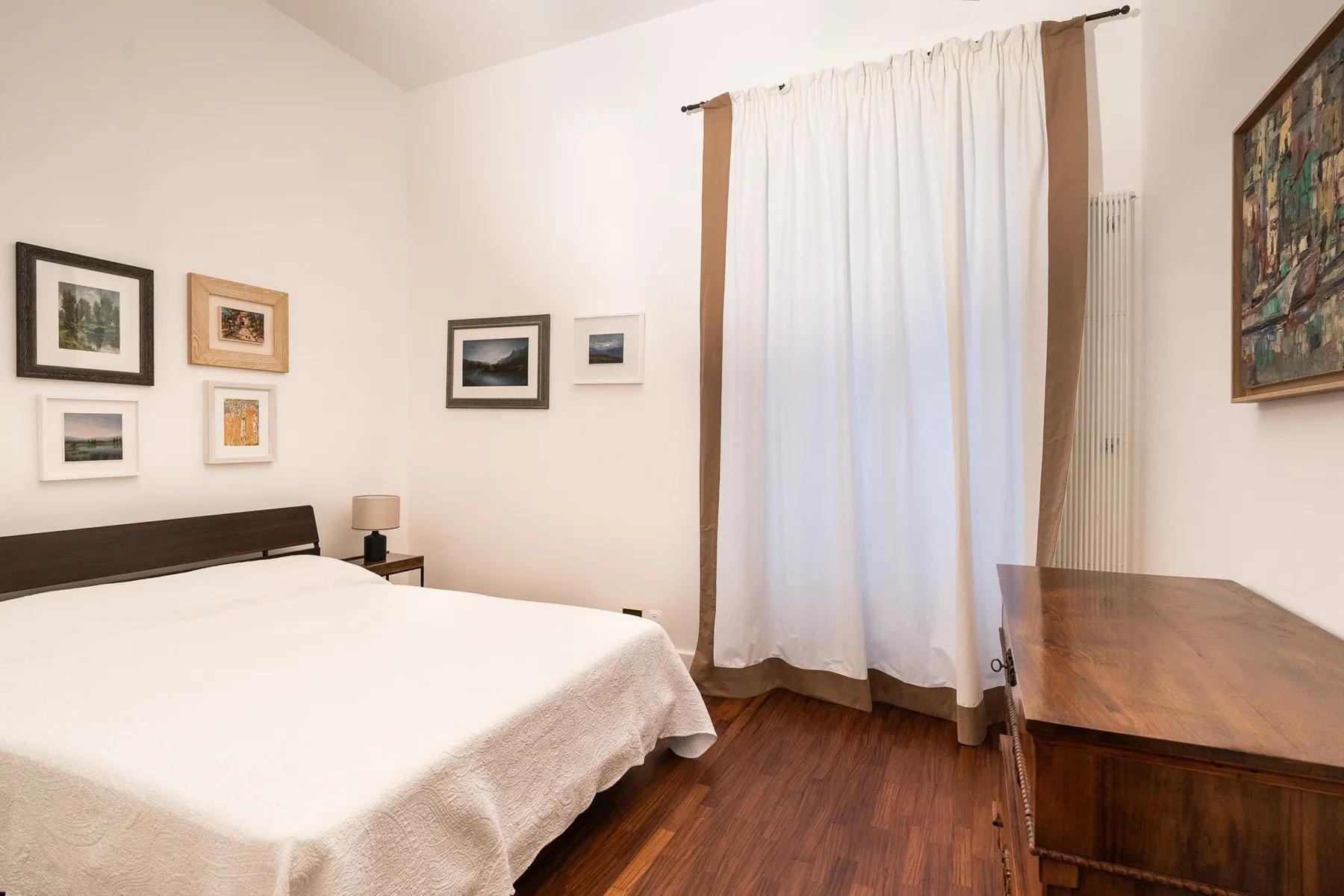 Un dormitorio con una cama tendida, cuadros enmarcados y un escritorio de madera.