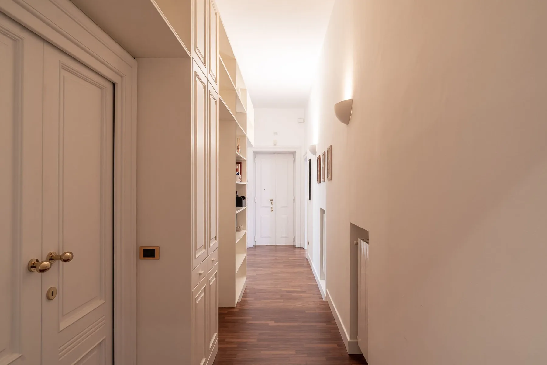 Un pasillo luminoso con armarios empotrados y suelo de tono madera.