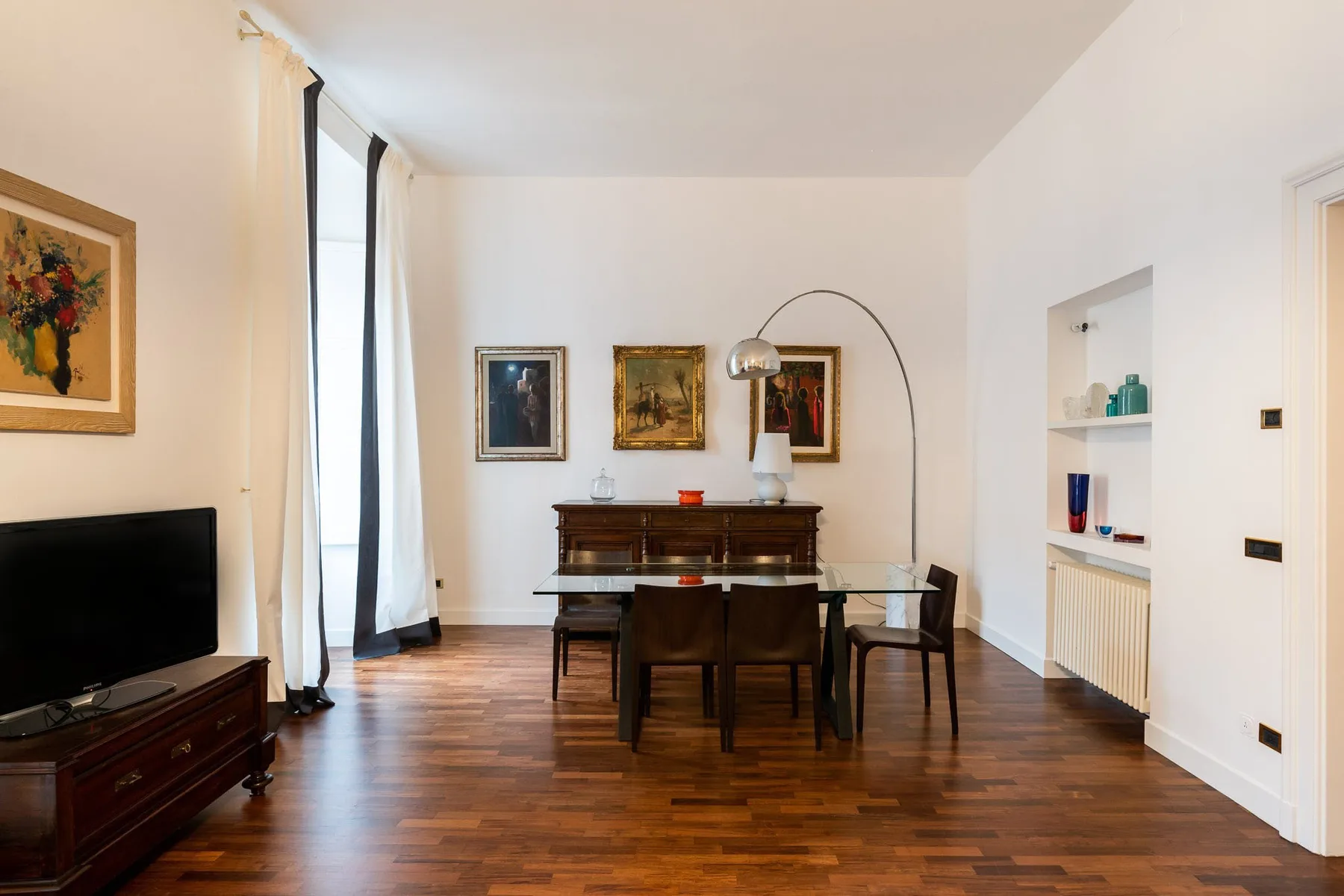 Comedor con una mesa de madera y sillas bajo una lámpara de pie curvada.