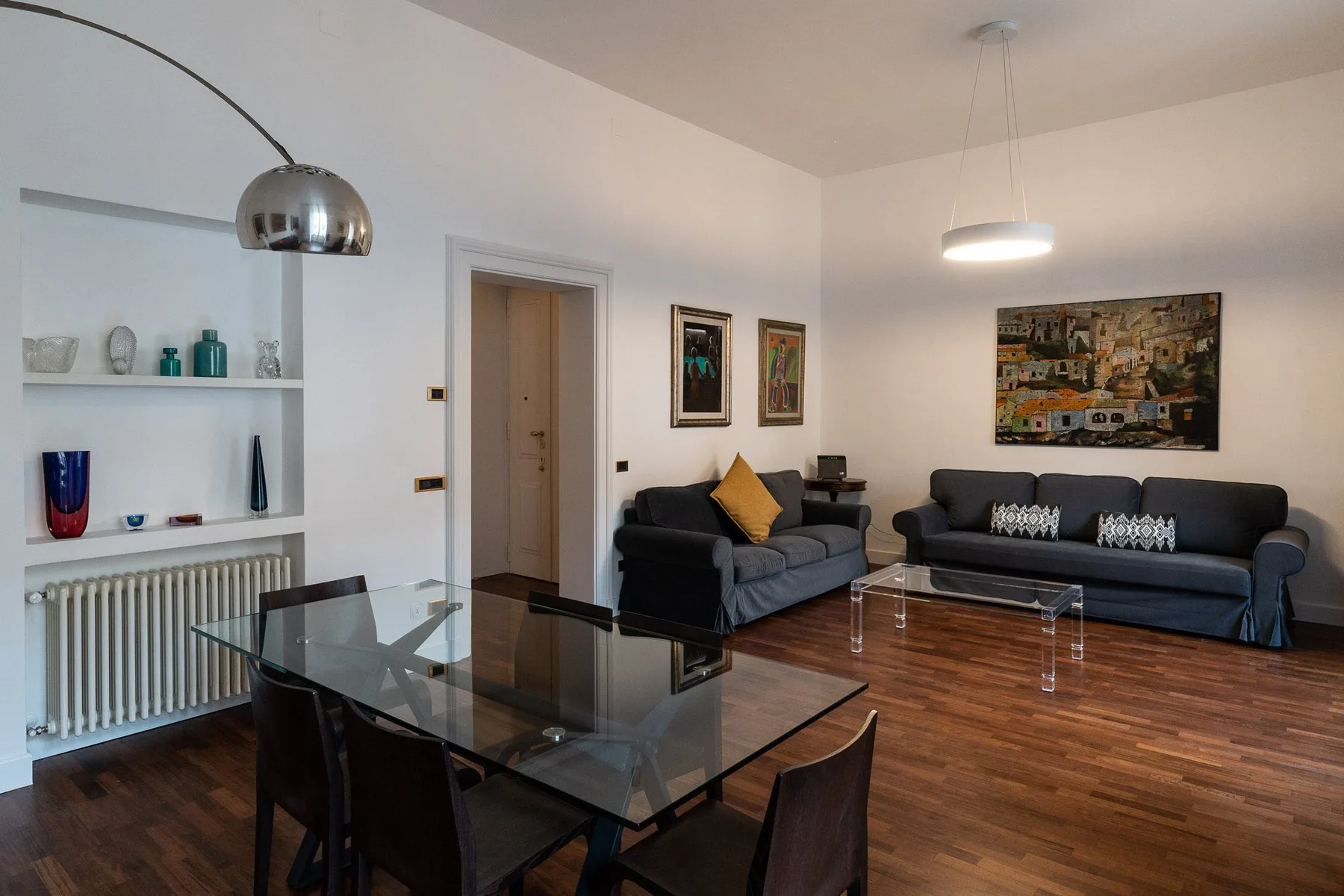 Una sala de estar con asientos oscuros, una mesa de centro de vidrio y una mesa de comedor.