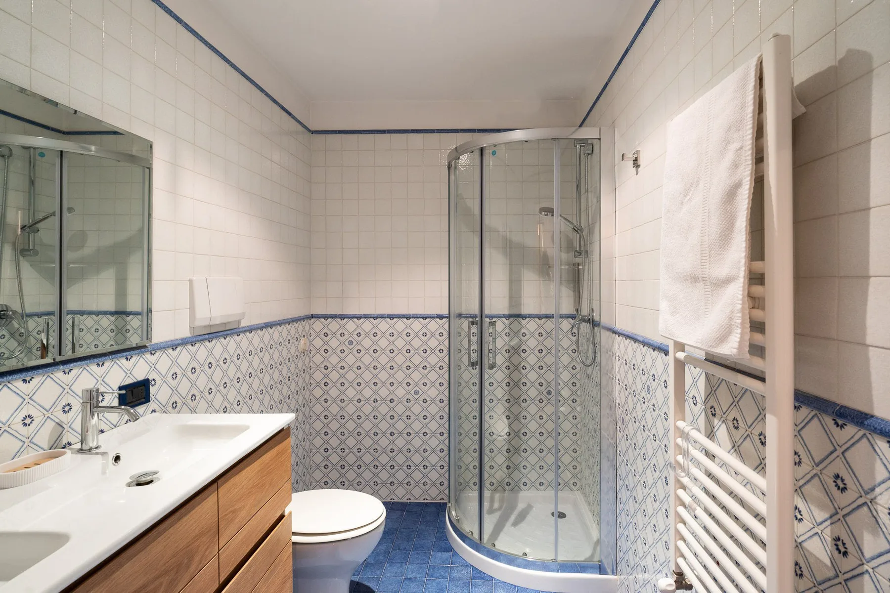 Un baño alicatado con ducha de vidrio, lavabo e inodoro.