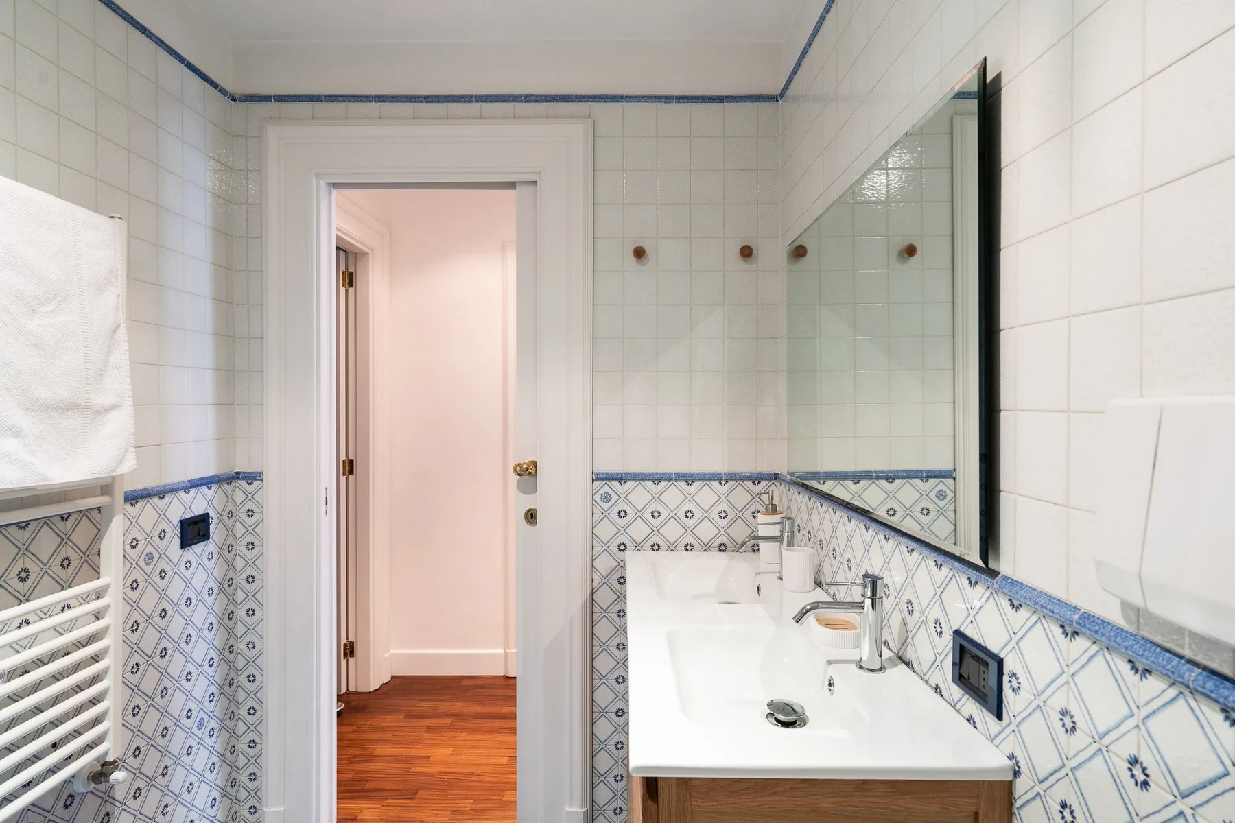 Un baño alicatado con lavabo, espejo y una puerta abierta.